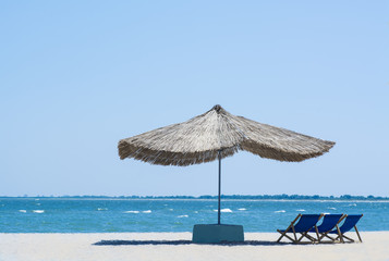 Beach straw umbrella from the sun on the beach with sun beds, on the background of the sea and blue sky