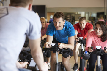 Instructor in foreground with spinning class at a gym - obrazy, fototapety, plakaty