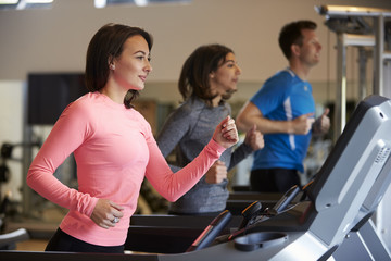 Fototapeta na wymiar Woman and two young adults running on treadmills at a gym