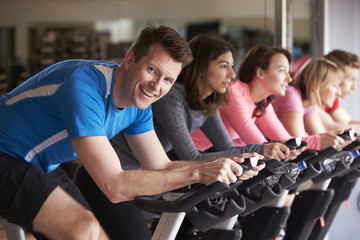 Man in a spinning class at a gym turning to smile at camera - obrazy, fototapety, plakaty