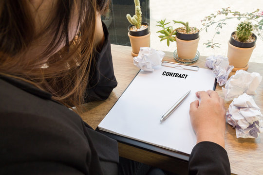 Stressed woman sitting at wooden desk with contract document