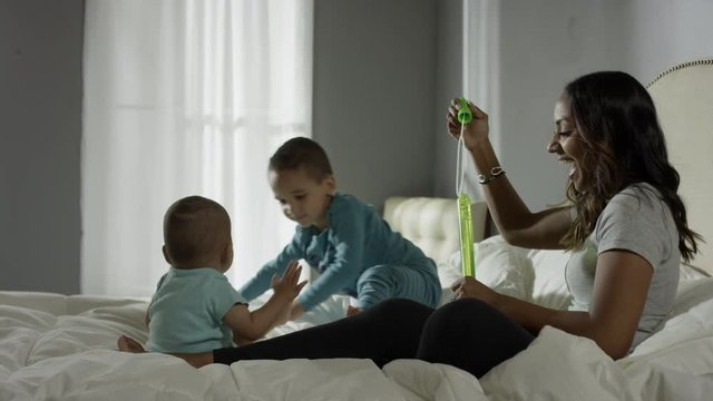 Medium panning shot of mother blowing bubbles for sons in bed / Cedar Hills, Utah, United States