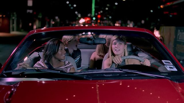 Four teenage girls cruising a nighttime street in a red convertible