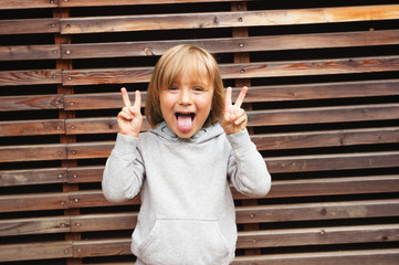 Fashion portrait of adorable toddler boy wearing grey sweatshirt, standing against wooden background