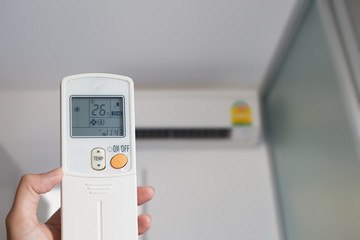 Left hand holding remote air conditioner turn up to 26 celcius with air conditioner blurred background