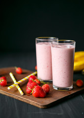 Strawberry and banana smoothie in the glass on black background