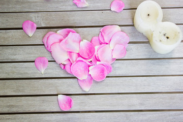 Petals of pink roses in a heart shape and a candle on a white wo