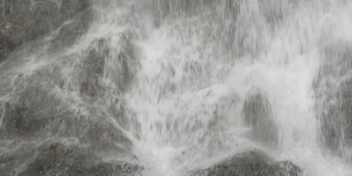 Close-up water pouring onto rocks at the foot of a powerful falls
