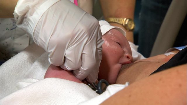 Close-up of baby at mother's breast; nurse checks infant's heart and lungs