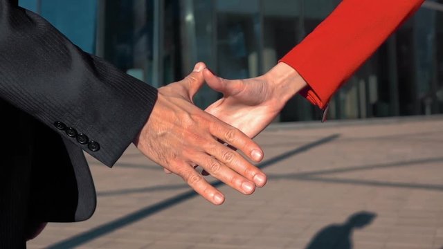 Slow motion: Young successful businessman and businesswoman shaking hands outdoor. teal and orange style. Glass modern business centre building bg. Close-up crane shot. Manicure