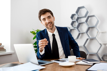 Naklejka premium Young successful businessman sitting at workplace, office background.