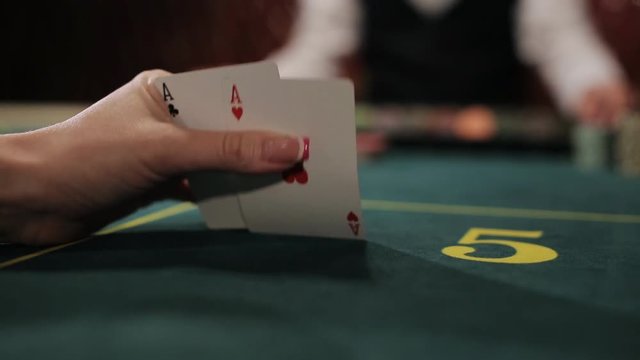 Stack of chips and two aces. POKER: The player's hand opens and looks his cards on a table