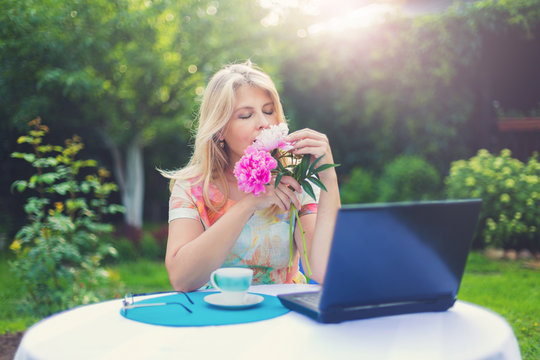 Красивая блондинка за чашкой кофе и ноутбуком в саду