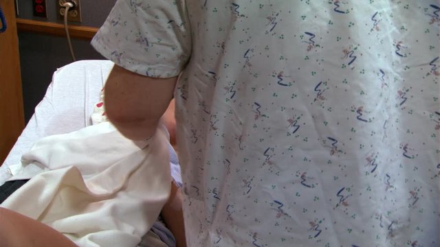 Young mother and newborn in hospital bed, nurse taking baby out of room