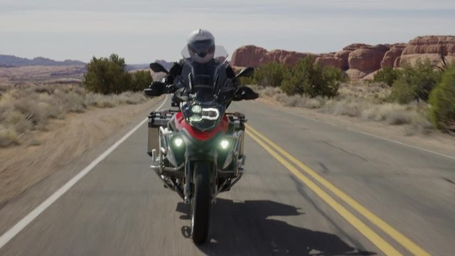 Medium tracking shot of man riding motorcycle on desert road / Arches National Park, Utah, United States