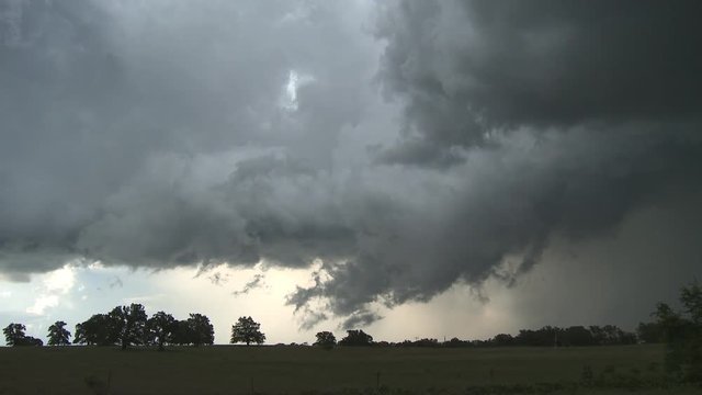 Storm clouds over a rural field, car passes on road in foreground