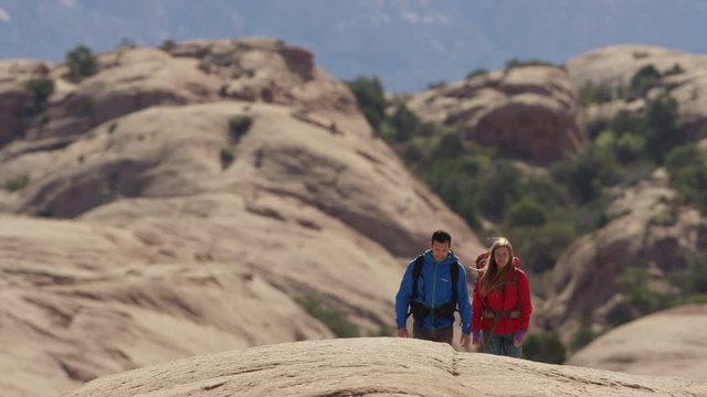 Wide panning shot of couple hiking in desert / Moab, Utah, United States