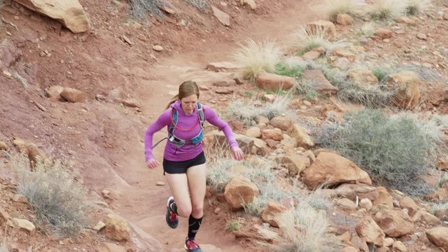 Wide slow motion high angle tracking shot of woman trail running in desert / Fisher Towers, Utah, United States