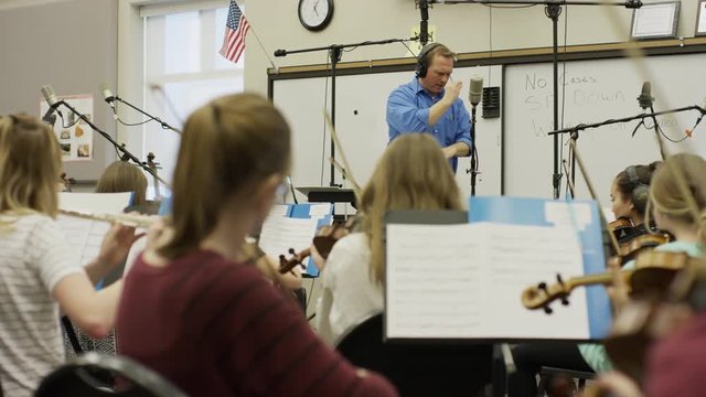 Medium panning shot of conductor leading school orchestra / American Fork, Utah, United States