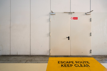 Fototapeta premium Emergency exit door with keep clear warning message on floor, copy space on wall