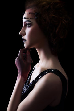 Fashion european model with unusual makeup and hairstyle and dress and red colored hand on black background.