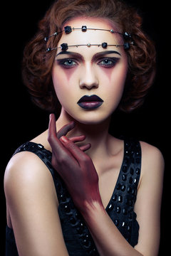 Fashion european model with unusual makeup and hairstyle and dress and red colored hand on black background.