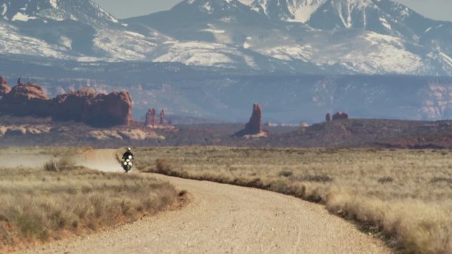 Wide shot of motorcycle approaching on desert road / Arches National Park, Utah, United States