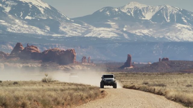 Wide shot of cars approaching on desert road / Arches National Park, Utah, United States