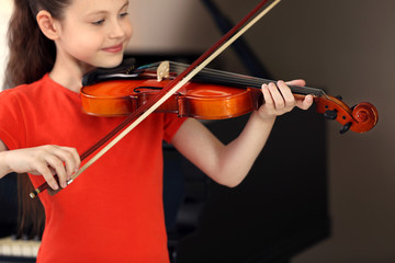 Little girl playing violin on piano background