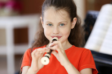 Little girl playing flute on piano background © Africa Studio