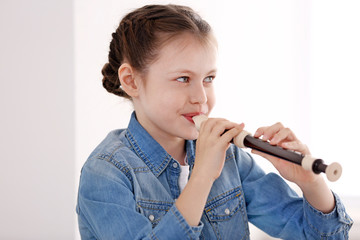 Little girl playing flute on light background © Africa Studio
