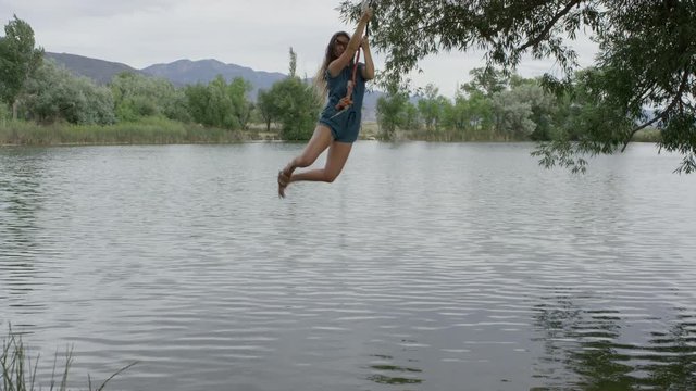 Wide slow motion panning shot of woman swinging into lake / Mona, Utah, United States