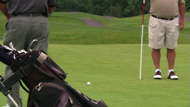 Golfer putting as companion removes flag stick, ball rolling into hole