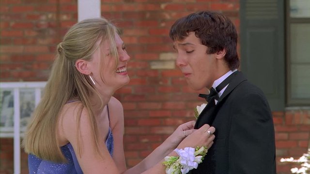 Teenage girl in prom dress pinning boutonniere onto lapel of escort's tux