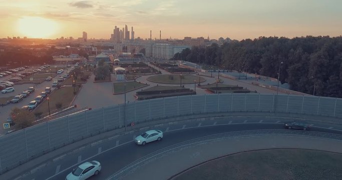 Aerial view of city traffic, road, public park, tops of the trees, Moscow River, and city skyline during sunset in Moscow, Russia.