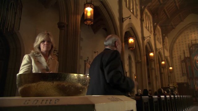 Man and woman dipping fingers into holy water before seating themselves in pews