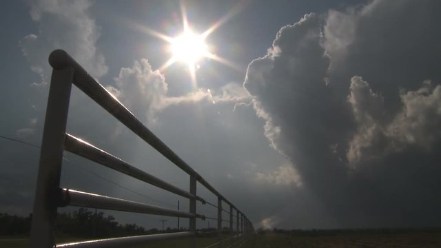 Sun glare among storm clouds over a pasture fence