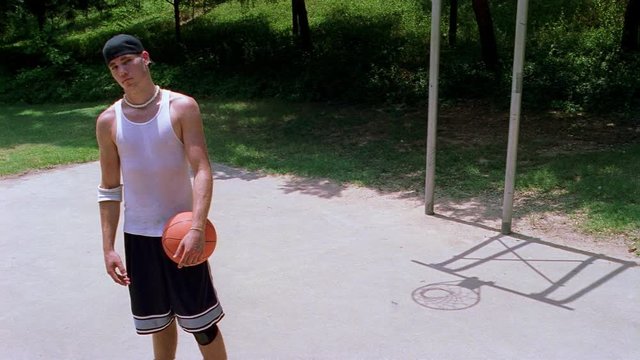 Unsmiling teen boy holding a basketball on an outdoor court