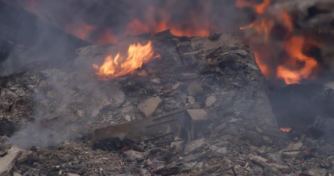 Close-up Low Flames Burning In Ash-covered Rubble After A Structure Fire