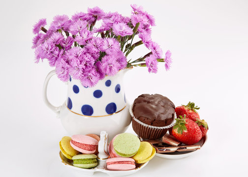 Flowers in vase with macaroons on saucer. Carnations and sweets.