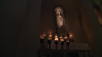 Woman kneeling before a statue of the Virgin Mary in a dimly lit church
