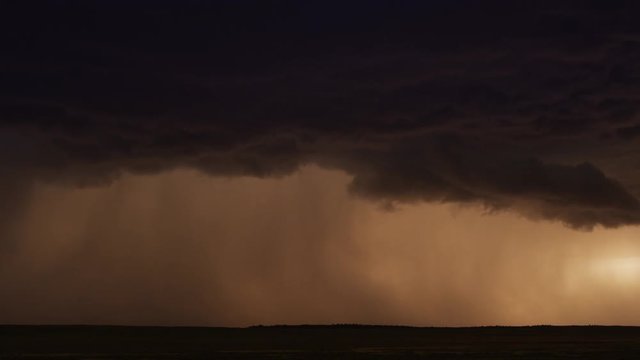 Lightning flashing from an advancing dark cloud as rain dims the sunset glow, time lapse