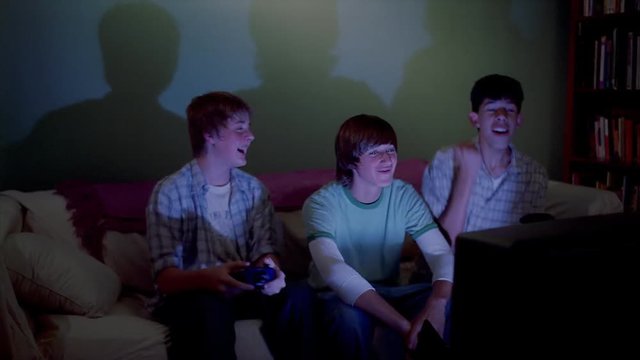 Three teenage boys playing an exciting video game in a shadowy living room