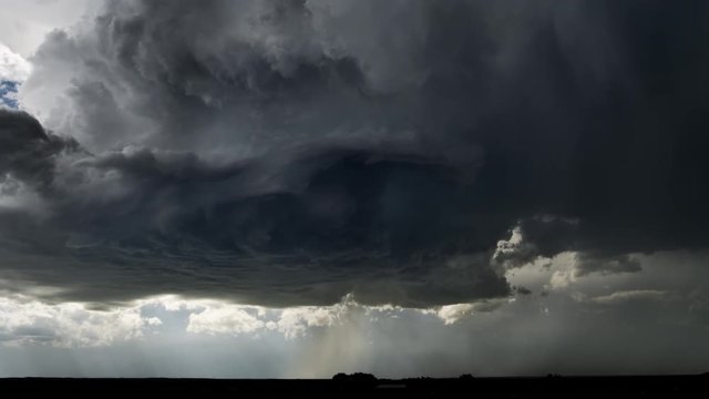 High-level base of a thunderstorm showing updraft and rotation, as hail pours onto a dark prairie landscape, time lapse