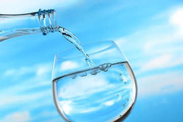 Fresh and clean drinking water being poured from bottle into glass on sky background