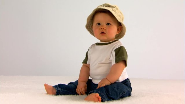 Seated baby boy in beige fishing hat