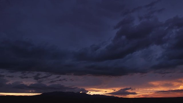 Purple and gold drifting clouds at sunset over mountains, time lapse