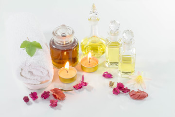 Obraz na płótnie Canvas Vintage old bottles of aromatic oils with burned candles, flowers, green maple leaf and white towel on glossy white table on white background, aromatherapy concept soft tone
