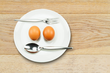 Two fresh eggs with fork and spoon on white plate on vintage  wooden table