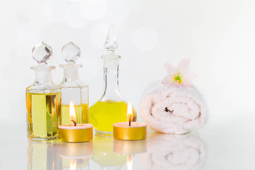 Vintage old bottles of aromatic oils with burned candles, flowers  and white towel on glossy white table on white background with bokeh, aromatherapy concept